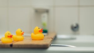 Image of three yellow toy ducks on a board across a bathtub